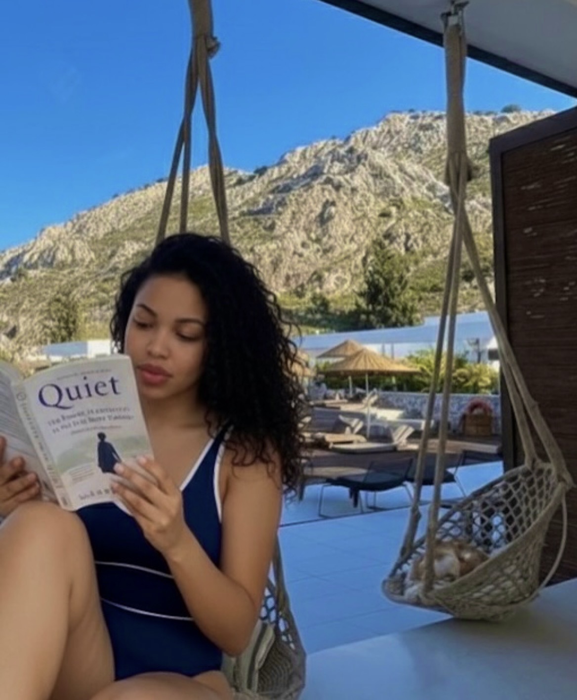 Lawrencia reading Quiet in a hanging chair outdoors
